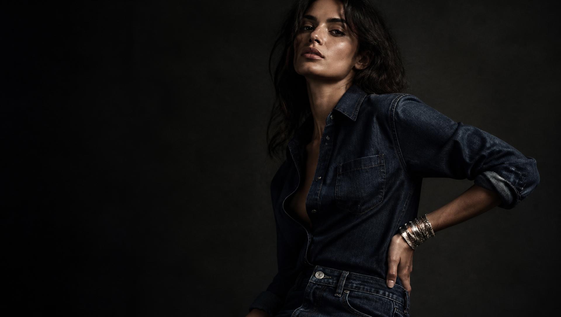 Modelo com camisa jeans escura e braceletes de prata em luz baixa